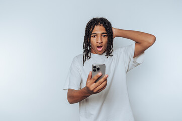 young man reacts with surprise while looking at his smartphone, showing a shocked expression on...