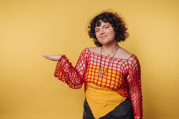 confident woman making a welcoming gesture in a bold, colorful outfit on yellow background