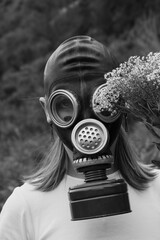 A woman in a gas mask holds a bouquet of small flowers, blending nature and protection