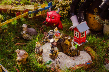 Whimsical garden scene in Nikiszowiec, Katowice, Poland, featuring small animal figurines, a red devil figure, and a tiny red house on white gravel.
