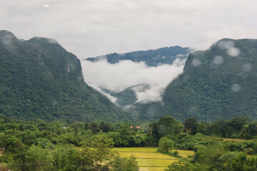Misty mountains and a verdant forest frame a waterfall shrouded in morning fog, a serene natural...
