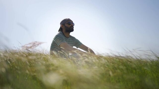 A man is sitting on the grass in a park, meditating or relaxing. Surrounded by lush greenery, the scene captures the natural beauty of a serene monsoon day in Rayta Hills, Udaipur, Rajasthan, India.