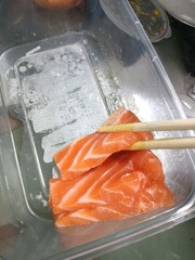 Salmon sashimi in a plastic container with chopsticks.
