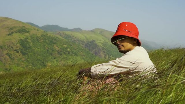 Portrait of a handsome teenage boy wearing a red hat, looking at the distant green hills at Rayta, Udaipur, India. A stylish fashion influencer standing outdoors.