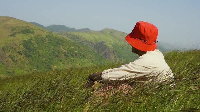 Portrait of a handsome teenage boy wearing a red hat, looking at the distant green hills at Rayta, Udaipur, India. A stylish fashion influencer standing outdoors.