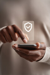 A close-up of a young Black man using a smartphone. He is tapping the screen, which displays a security icon. The background is neutral and soft.