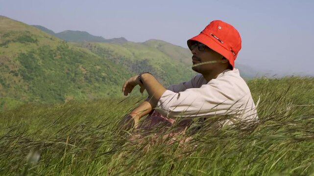 Portrait of a handsome teenage boy wearing a red hat, looking at the distant green hills at Rayta, Udaipur, India. A stylish fashion influencer standing outdoors.