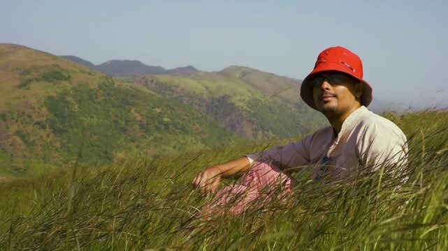 Portrait of a handsome teenage boy wearing a red hat, looking at the distant green hills at Rayta, Udaipur, India. A stylish fashion influencer standing outdoors.
