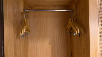 The interior of a modern wooden wardrobe shows a metal hanging rod with two empty wooden hangers....