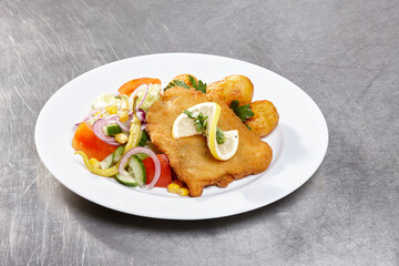 A delicious plate features crispy fried fish garnished with lemon, accompanied by a vibrant salad of fresh vegetables and fried potatoes, showcasing a hearty meal