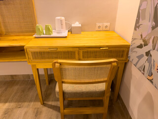 A cozy wooden desk with rattan drawers sits in a well-lit room, featuring a kettle, cups, and a chair, ideal for a comfortable workspace or refreshment nook