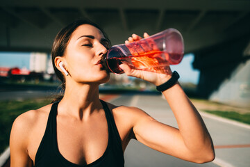 Young sporty woman drinking water after training outdoors