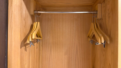 The interior of a modern wooden wardrobe shows a metal hanging rod with two empty wooden hangers....