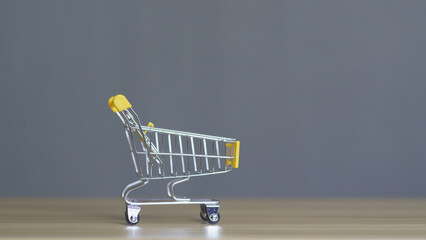 Mini shopping cart with yellow accents on a wooden table against a gray background, symbolizing...