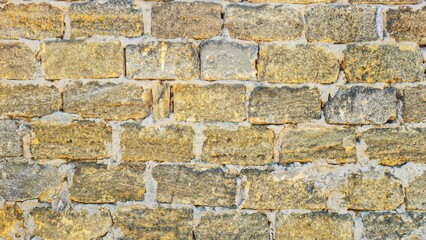 Old stone wall made of yellow and grey rough-cut bricks with visible mortar. Texture background of weathered masonry. Architecture and construction detail