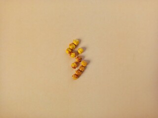 A scattered arrangement of small, golden-yellow gourds, or roasted chickpeas on a plain beige...