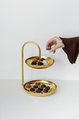 A woman takes dessert from a golden shelf. Handmade chocolates or cheese truffles on a golden...