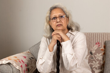 Indian sad  and depressed senior woman grandmother sitting on the wooden chair at home. ...