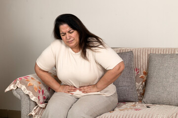 Indian plus size woman suffering for stomach 
and menstrual pain sitting on sofa at home