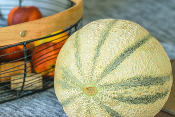 Freshly harvested melon with a basket of assorted fruits on a textured surface