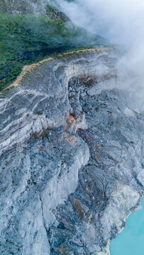 Aerial view of the rugged terrain and sulfuric mist mingling with the vibrant turquoise lake at the base of the Ijen Volcano Crater, East Java, Indonesia.