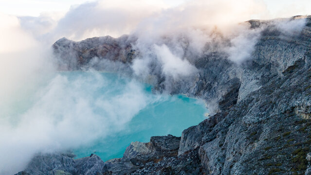 Aerial view of the turquoise crater lake nestled amidst rugged cliffs and swirling mist, Ijen Volcano Crater, East Java, Indonesia.