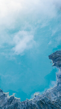 Aerial view of the turquoise crater lake nestled within the rugged Ijen Volcano, a mesmerizing contrast against the stark, rocky terrain, Ijen Volcano Crater, East Java, Indonesia.
