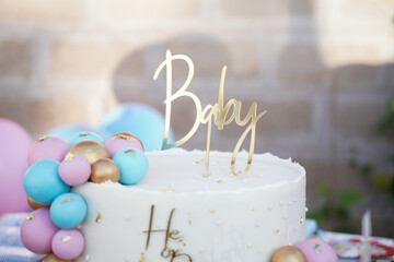 Elegant gender reveal cake decorated with pastel balloon accents, gold flakes, and a stylish “He...