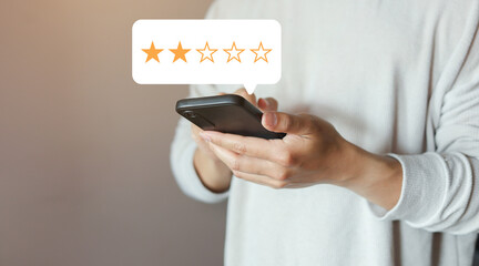 close up on customer man hand use smartphone and pressing two star (poor rating) feedback rank for give score point to review the service and experience on business concept