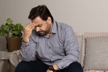 Portrait of indian sad depressed man sitting on sofa in living room at home alone suffering from...