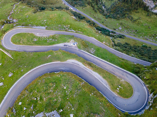 winding mountain road curves of a high altitude alpine pass in green summer scenery, aerial view