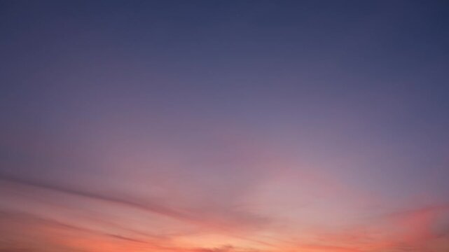 A calm sunrise sky timelapse with soft orange and pink streaks spreading gently across a purple and blue sky, creating a peaceful and hopeful start to the day with warm, glowing hues. Time-lapse.
