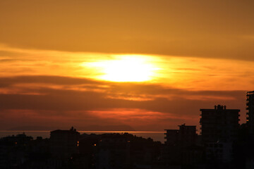A beautiful sunset casting warm colors over a coastal city and calm sea, creating a serene atmosphere.
