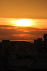 A breathtaking sunset over a coastal city, where golden and orange hues blend seamlessly with the...