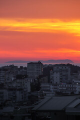 Golden sunset over a seaside city, with calm water reflecting the colorful sky.

