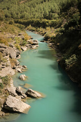 A vibrant blue lagoon river flowing through a mini canyon surrounded by green forest, creating a...