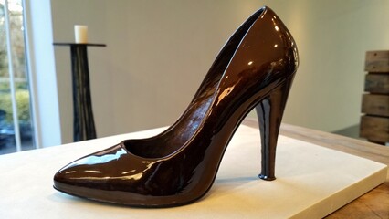 A glossy chocolatebrown high heel shoe sculpture is displayed on a table, showcasing its elegant...