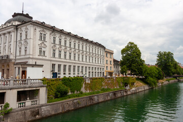 A picturesque view along the Ljubljanica River in Ljubljana, features elegant historical buildings...