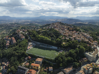 Aerial view of the vibrant green sports field nestled among the old buildings on the hilltop, contrasted against the blue sky, Ariano Irpino, Avellino, Italy.
