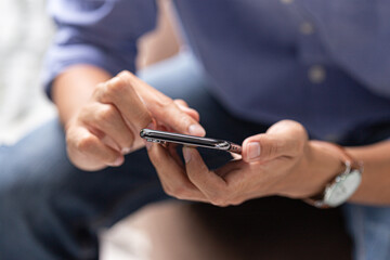 Close-up of man using smartphone with both hands, casual blue shirt, modern communication and digital lifestyle concept.