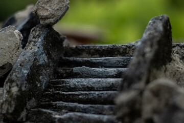 Ancient stone steps leading upwards against a blurred green garden background. A conceptual image...