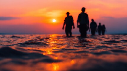Silhouettes of people walking through shallow water during a vibrant orange sunset reflecting on the ocean surface.