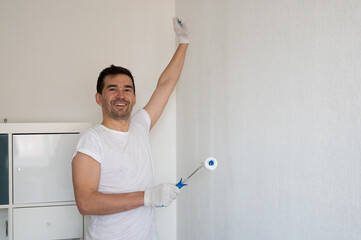 Happy painter smiling and painting a white wall with a paint roller, home renovation and interior design concept