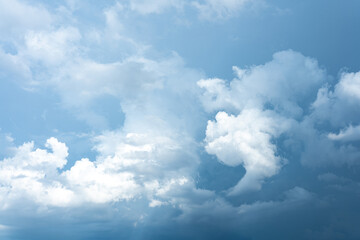 Dynamic sky presenting a mix of bright white and dark gray cumulus clouds against a pale blue...