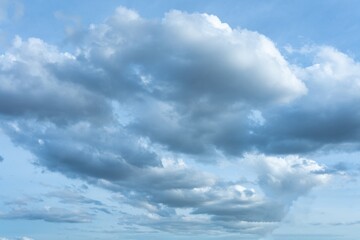 Fluffy white and dark grey storm clouds float across a bright blue daytime sky creating a dynamic...