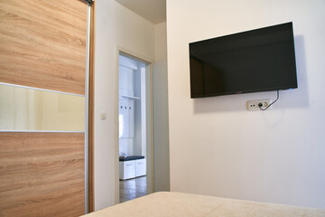Wall-mounted flat screen tv in modern bedroom with wooden furniture and neutral decor