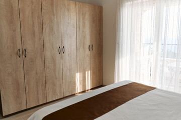 Sunlit bedroom with wooden wardrobe and bed near window