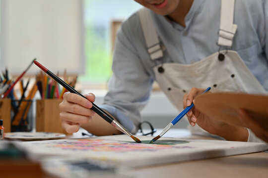 Close-up of two artists painting together on a shared canvas, blending creativity and teamwork in a studio