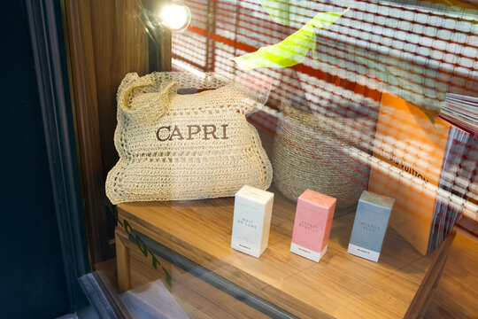 Siracusa, Italy - June 28, 2025: Stylish woven bag with 'Capri' branding and elegant cosmetic boxes displayed in a boutique window of Alcott