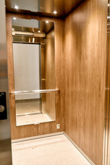 Modern wood-panel elevator interior with mirror and bright lighting © Lui Shtein